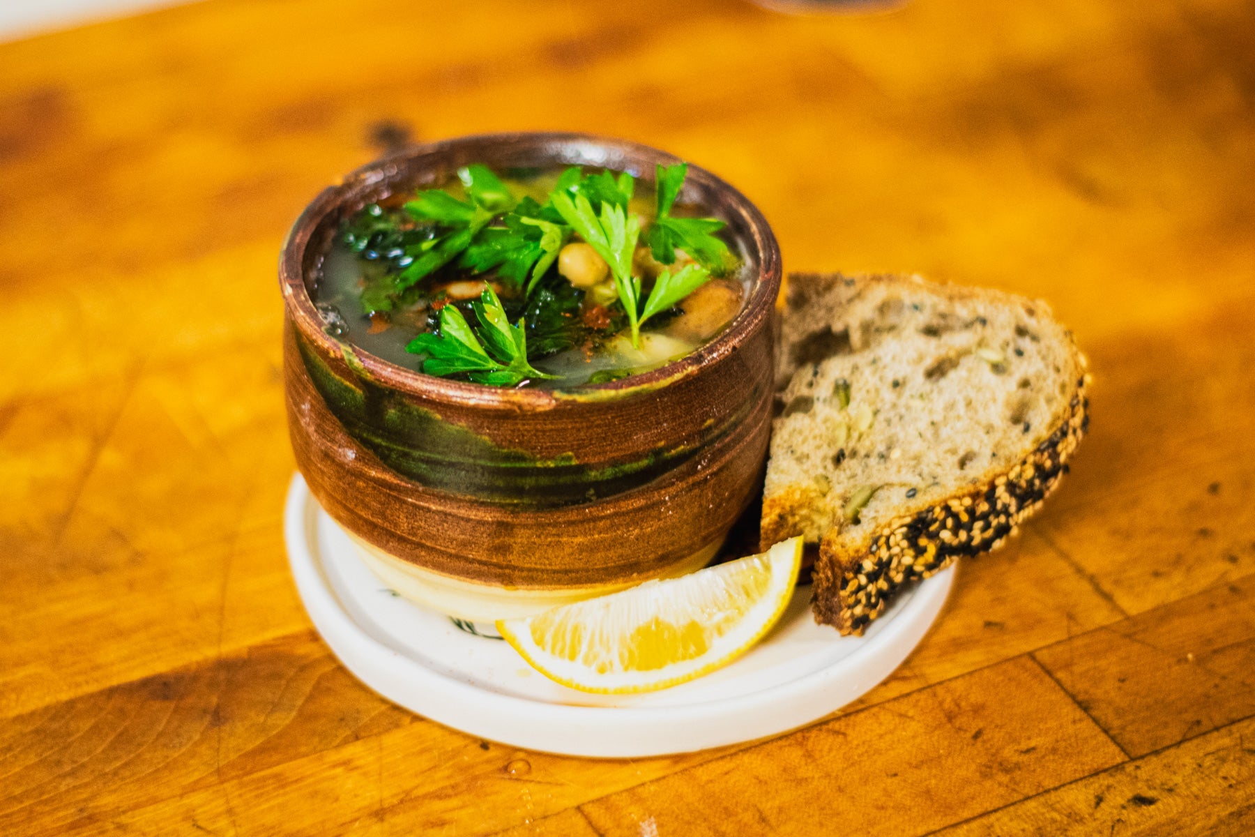 Rustic tuscan soup in a handcrafted ceramic bowl with a wedge of lemon and a slice of seeded bread.