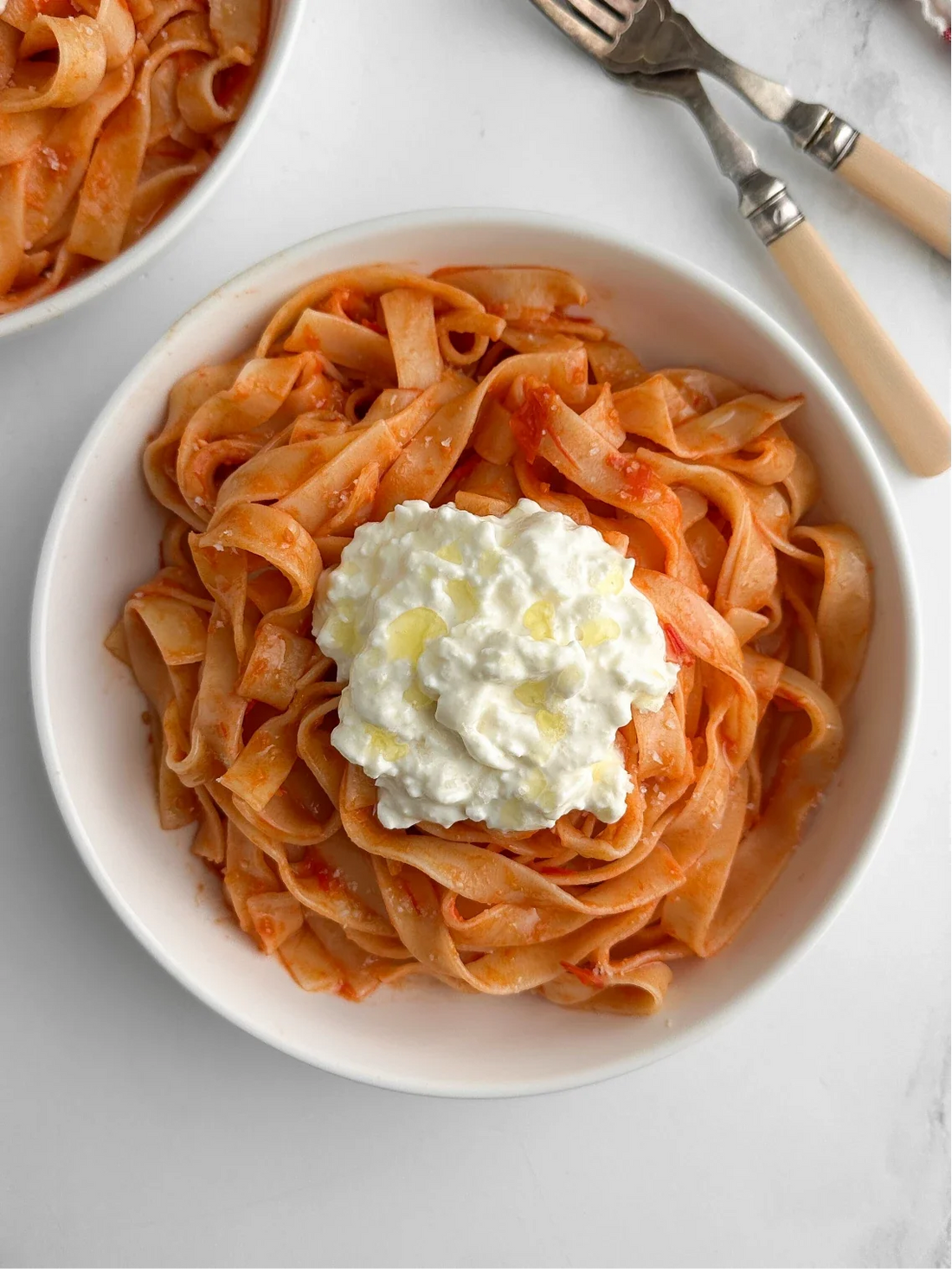 Photograph of two bowls of Sungold tomato pasta with stracciatella and Meyer lemon olive oil. Photograph in the background is only partially in the shot.