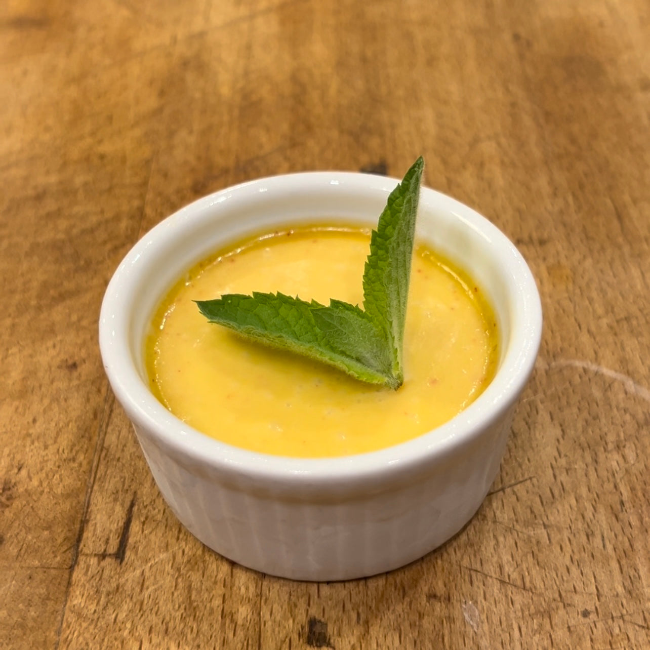 A petite ramekin of peach and olive oil gelato, garnished with a fresh mint leaf.