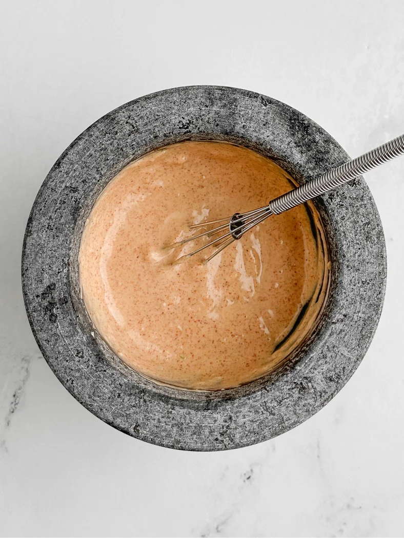 Photograph taken from above of a molcajete filled with garlic lemon mitmita aioli and a small metal whisk
