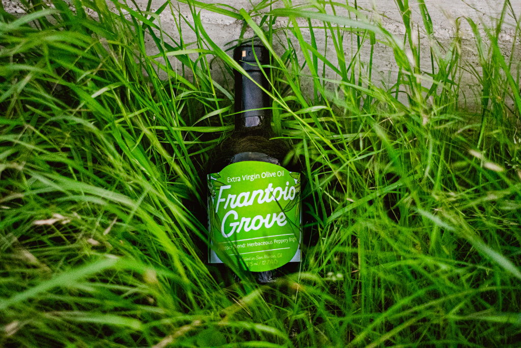 Bottle of Frantoio Grove EVOO in a field of grass
