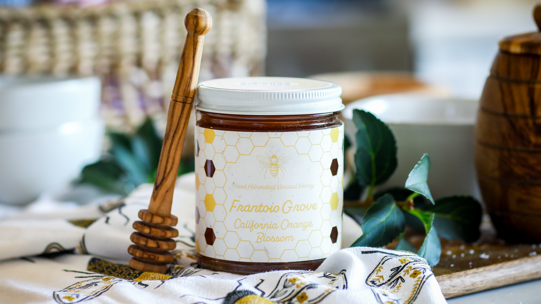 A Jar of Orange Blossom Honey Sitting On a tablecloth with a honey wand, in the background is a honey jar