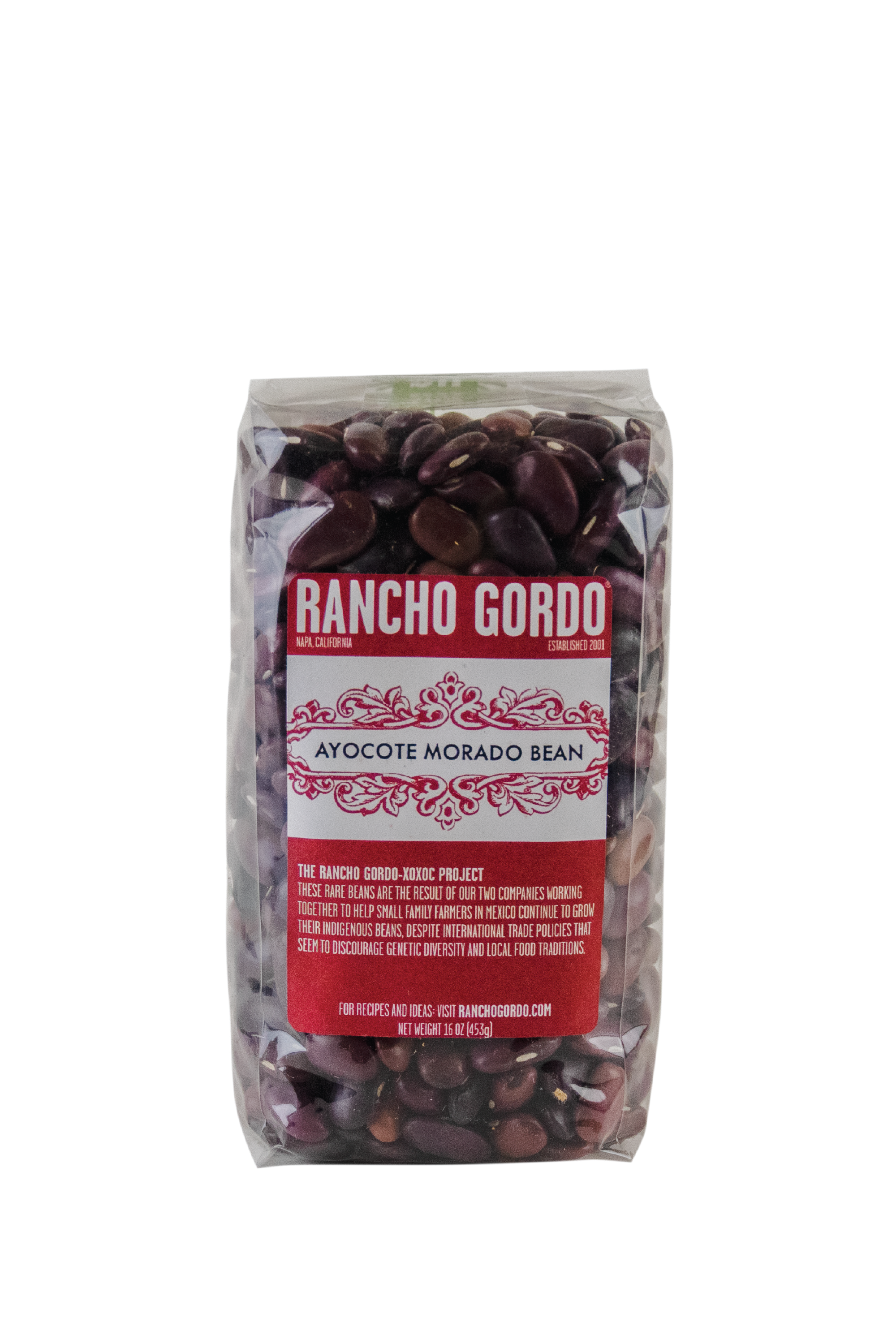 A One Pound Bag of Rancho Gordo Acoyote Morado Beans on a white background. Red and white label. Additional text on bag reads: The Rancho Gordo-Xoxoc Project. These rare beans are the result of our two companies working together to help small family farmers in Mexico continue to grow their indigenous beans, despite international trade policies that seem to discourage genetic diversity & local food traditions.