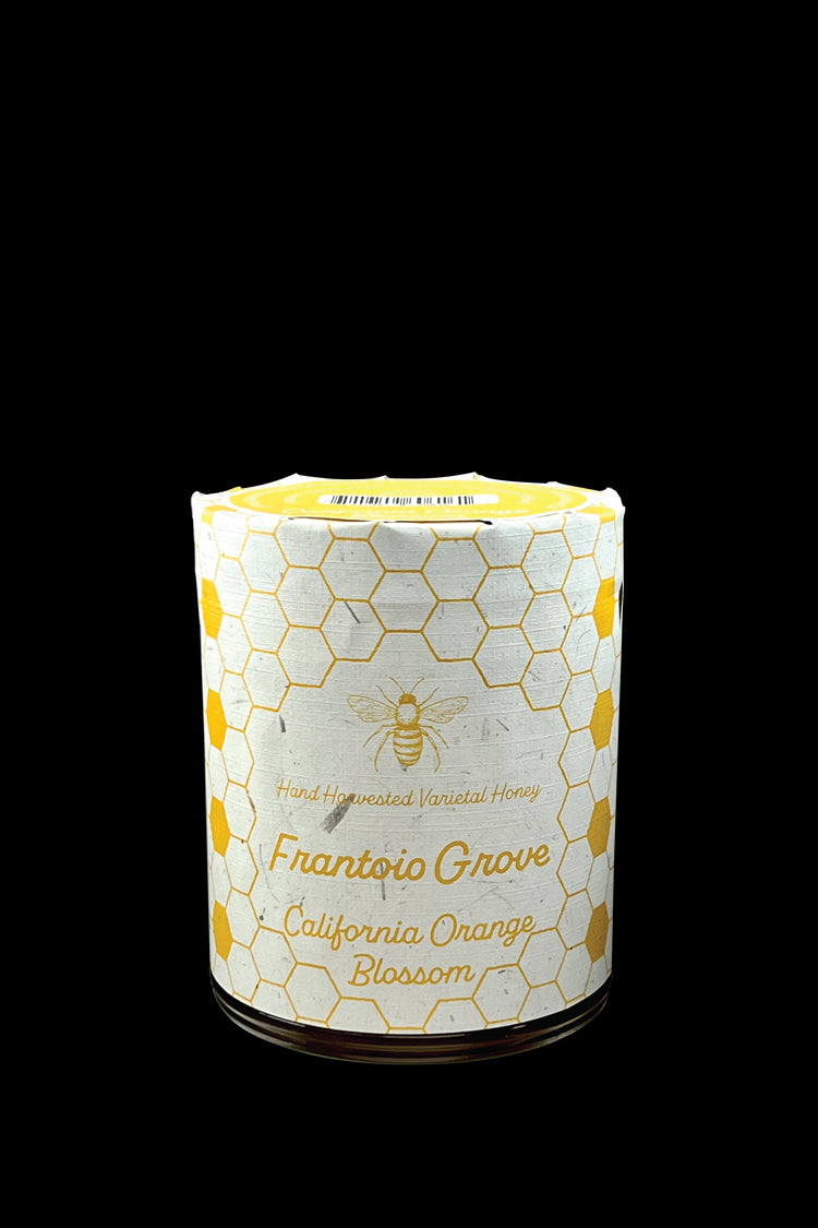 Image of a jar of Frantoio Grove's hand harvested California Orange Blossom Honey on a White Background. Jar is wrapped in white paper with art depicting a bee and a pattern of alternating yellow and white honeycomb.
