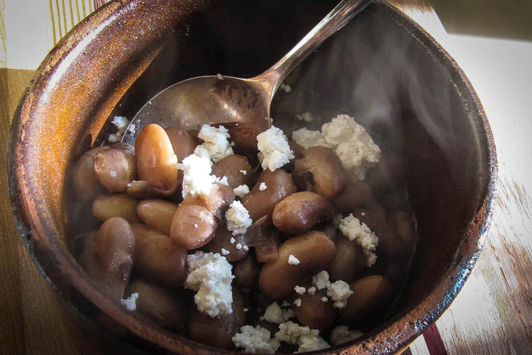 A picture of cooked Snowcap beans, topped with queso fresco in an earthenware bowl with a silver spoon.