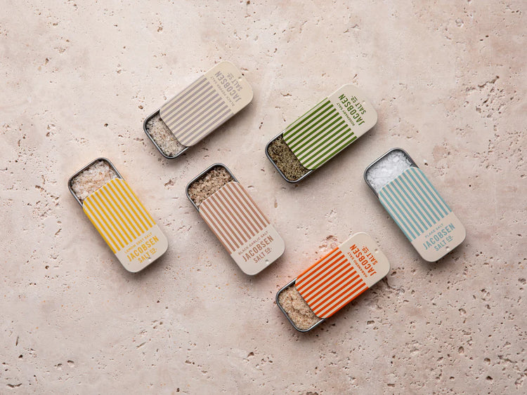 Set of six Jacobsen Salt Co's slide tins arranged in alternating rows on a stone surface.