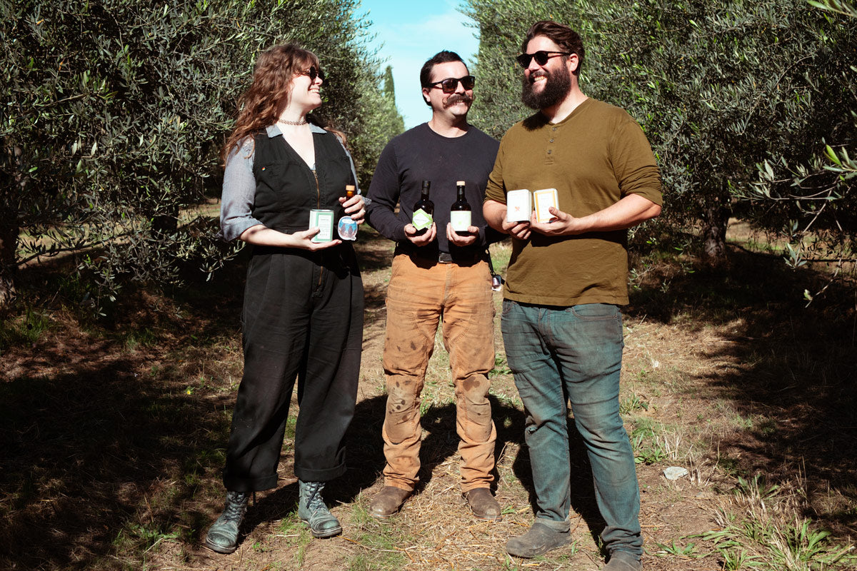 Three members of the Frantoio Grove team with products in the olive orchard.