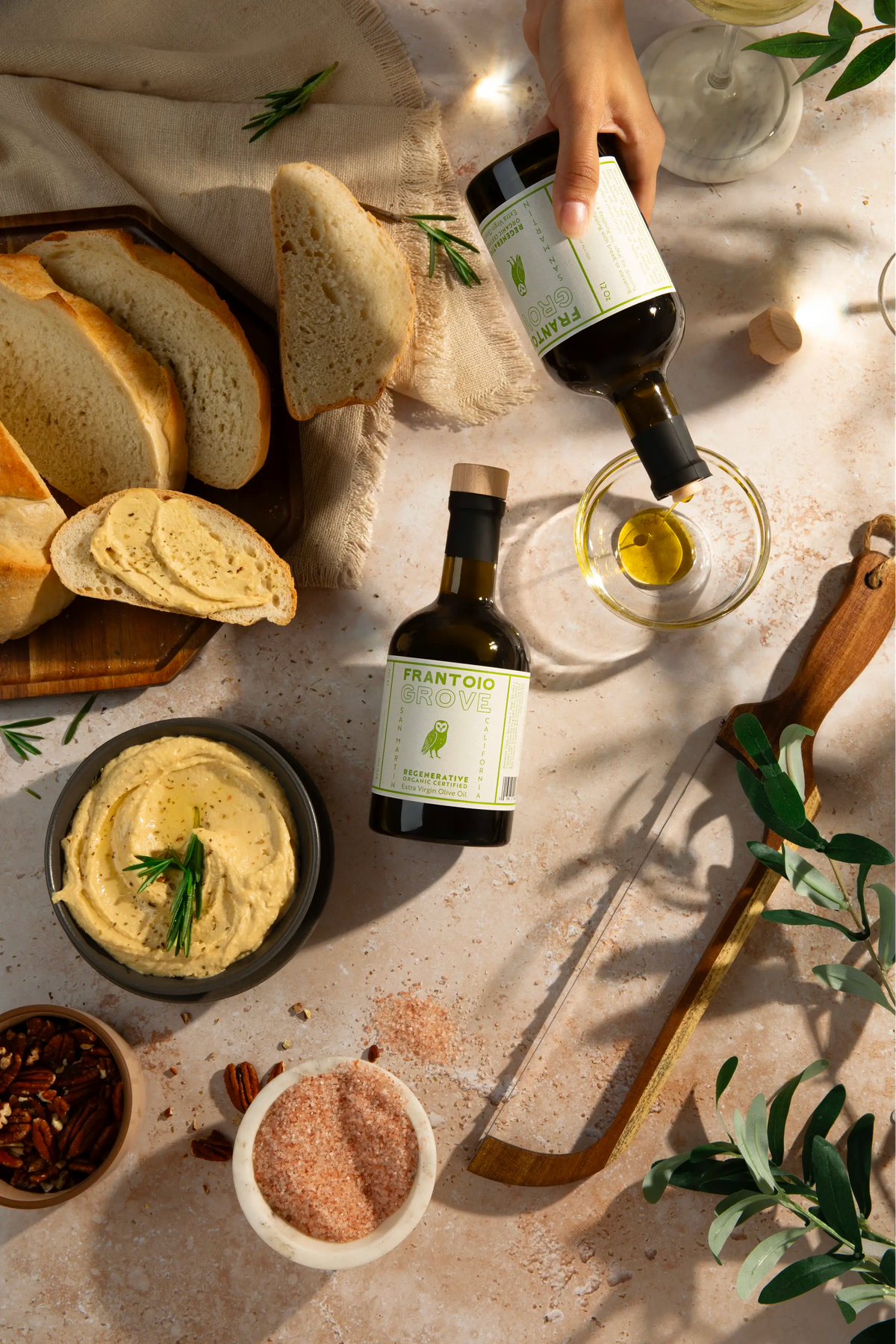Frantoio Grove olive oil being poured beside bread, hummus, and linen.