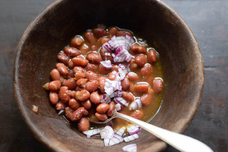 A picture of cooked King City Pink beans topped with finely chopped red onions in an earthenware bowl with a silver spoon.