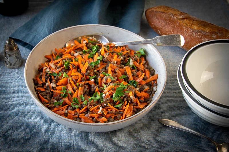 An Image Showing a Salad Made From French Green Lentils and Shaved Carrots, Dressed With Parsley and Served With a Side of French Bread.