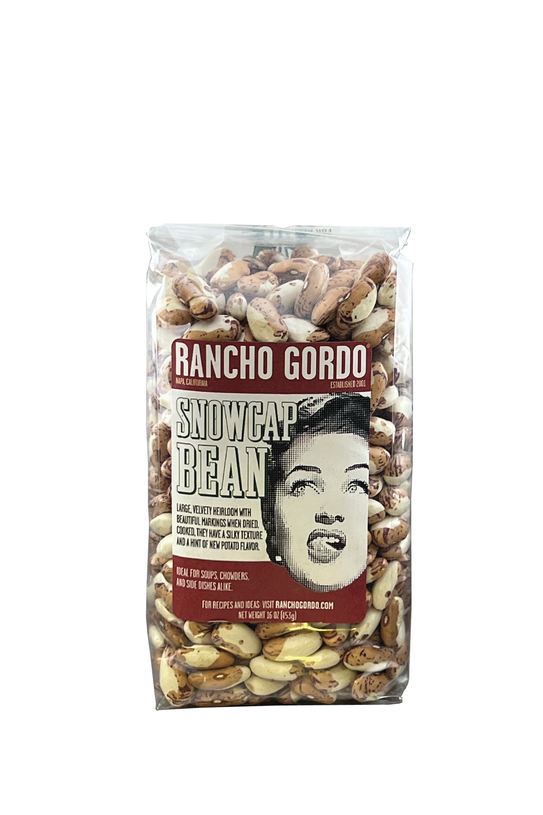 A One Pound Bag Of Rancho Gordo Snowcap beans on a white background. Red and white label with an image of the face of a woman licking her upper lip. Additional text on bag reads: Large, velvety heirloom with beautiful markings when dried. Cooked, they have a silky texture and a hint of new potato flavor. Ideal for soups, chowders, and side dishes alike.